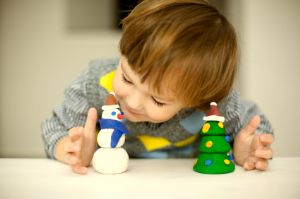 Young boy playing with a clay snowman and a clay tree.